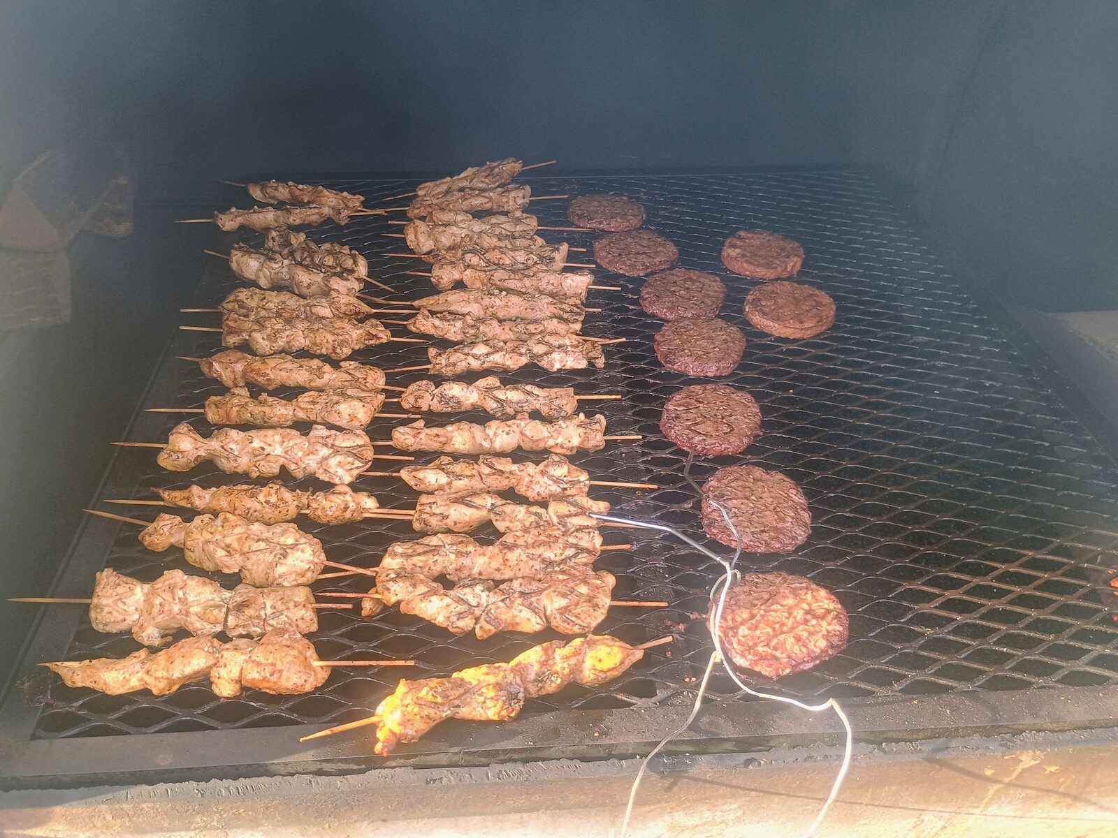 Inside the smoker — kebab skewers and burgers on the grate, temperature probe visible